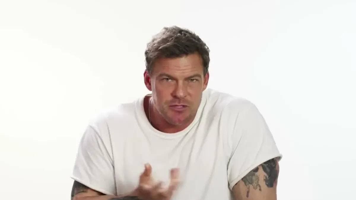 Alan Ritchson in a white T-shirt, looking at the camera during an interview