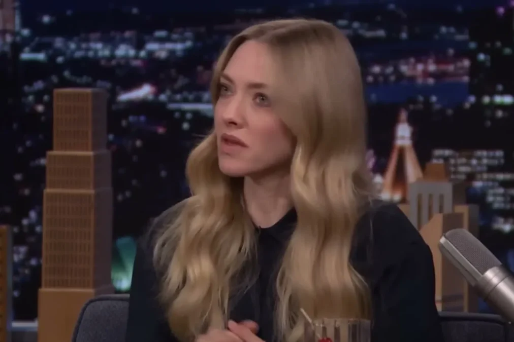 Amanda Seyfried in a dark collared shirt talking during a late-night talk show interview