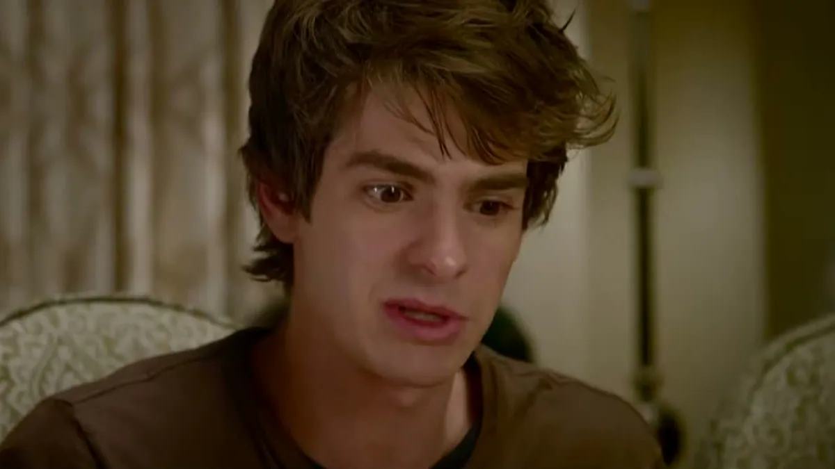 Andrew Garfield as a young Peter Parker sitting in a living room in The Amazing Spider-Man