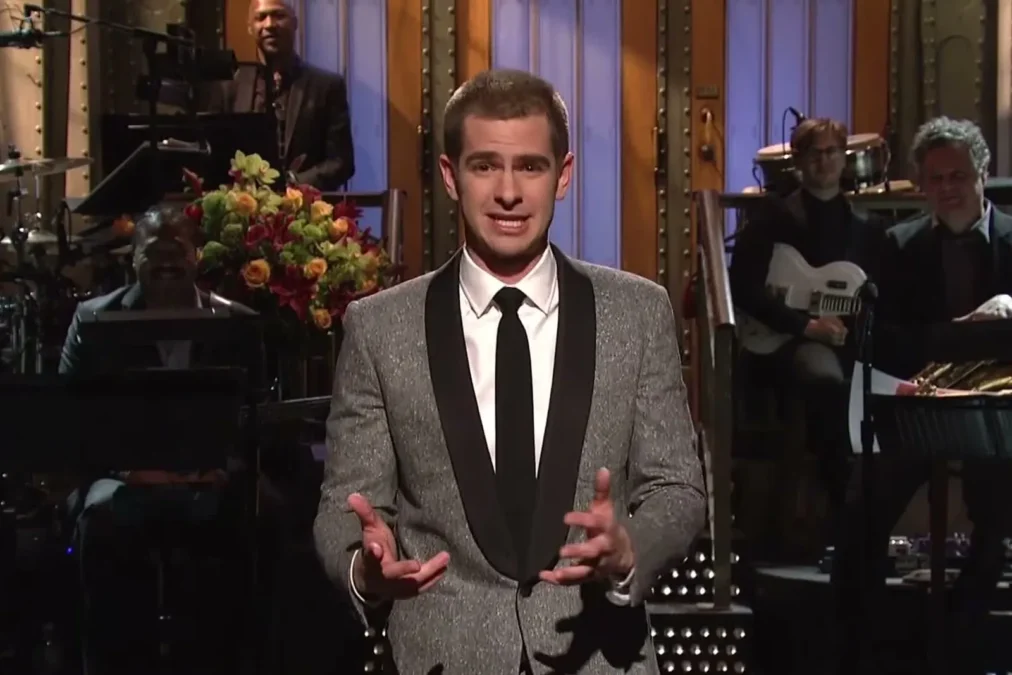 Andrew Garfield in a gray tuxedo jacket and black tie delivering the monologue on the Saturday Night Live stage