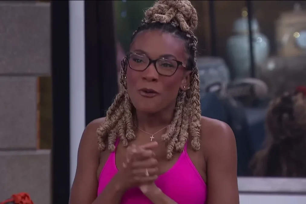 Taylor Brown in glasses and a pink top, speaking with her hands clasped in the Big Brother house