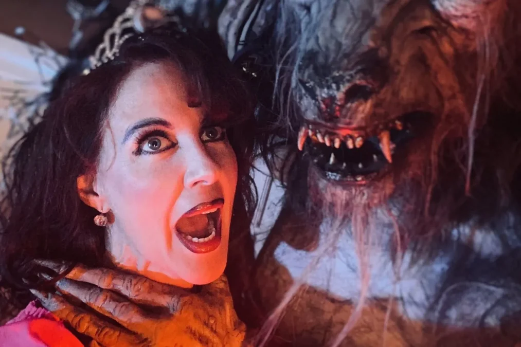Amber Arnett-Bequeaith, wearing a tiara and red top, screams in mock fright as a werewolf character from the Beast grips her neck