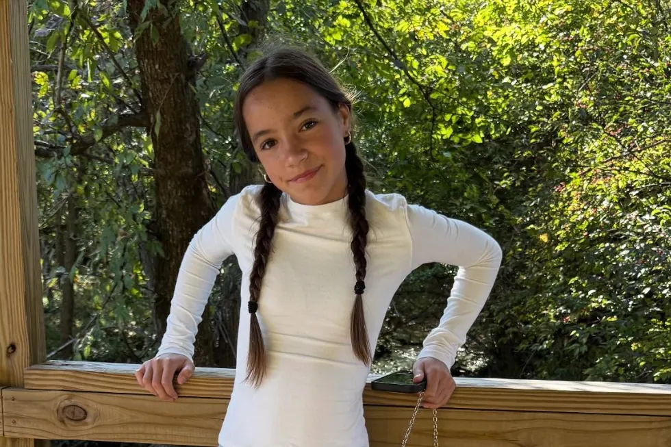Fiona Lowe smiling in a white long-sleeve top with her hair in two braids, leaning on a wooden railing outdoors
