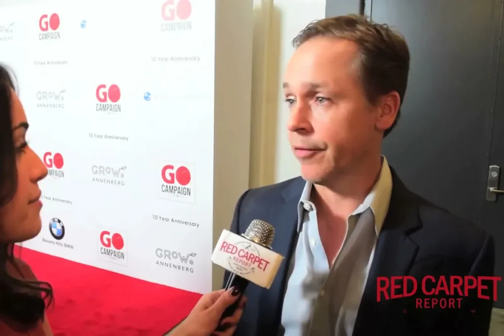 Chad Lowe in a navy blazer talking to a reporter on a red carpet