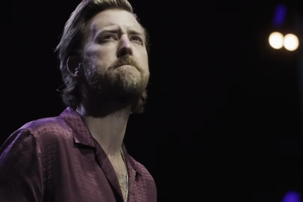 Charles Kelley in a burgundy shirt looking up on a dark stage during a live performance