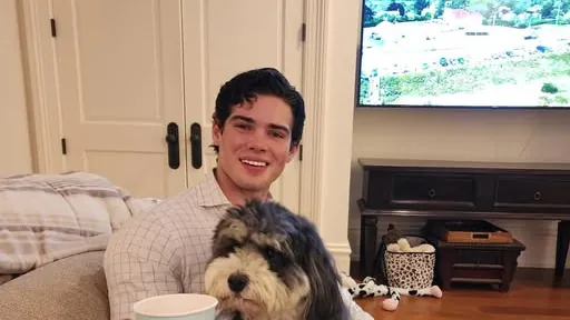Braden Peters, known online as Clavicular, smiling at home with his dog