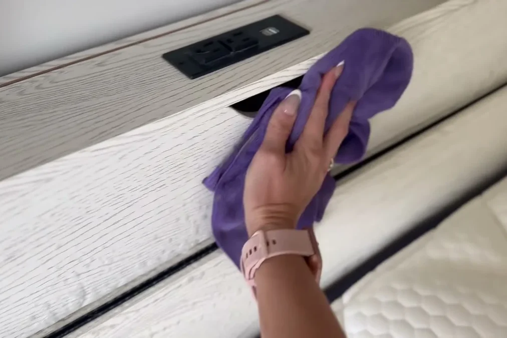 A hand wiping a white headboard with a purple microfiber cloth