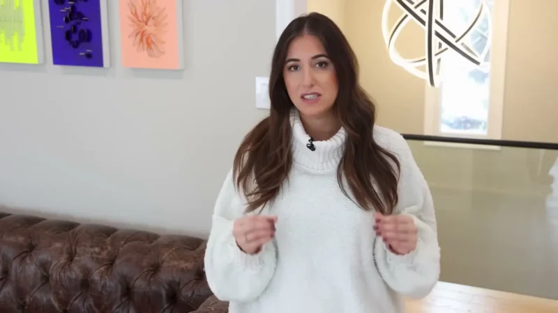 A cleaning YouTuber in a white turtleneck sweater explaining a cleaning schedule in her living room