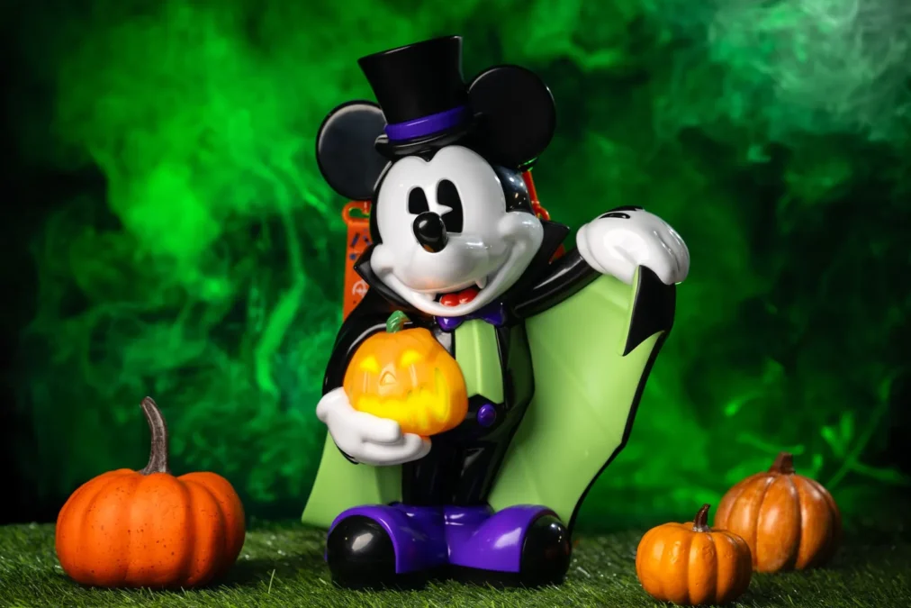 The Vampire Mickey Mouse popcorn bucket, Mickey in a black top hat and green cape holding a glowing jack-o'-lantern, among small pumpkins