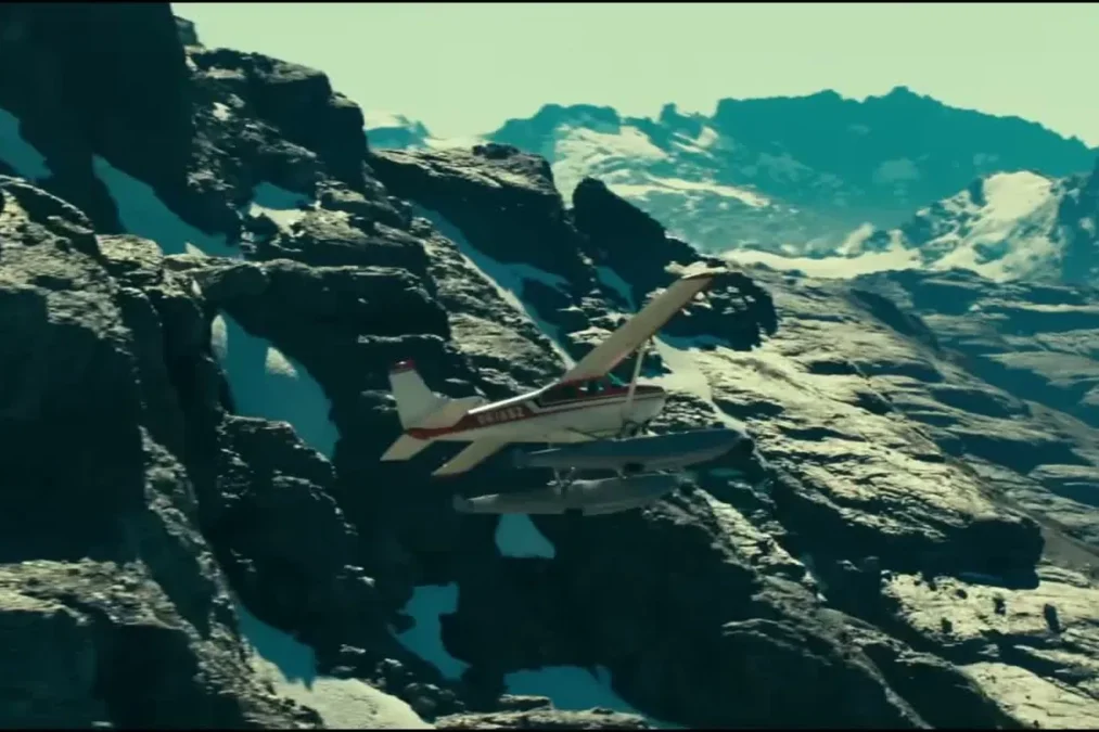 A small seaplane flying low over snowy, rocky mountains in Heart of the Beast
