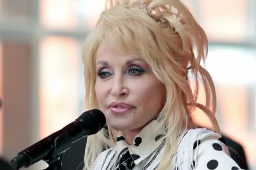 Dolly Parton in a platinum updo and a polka-dot collar, speaking into a microphone