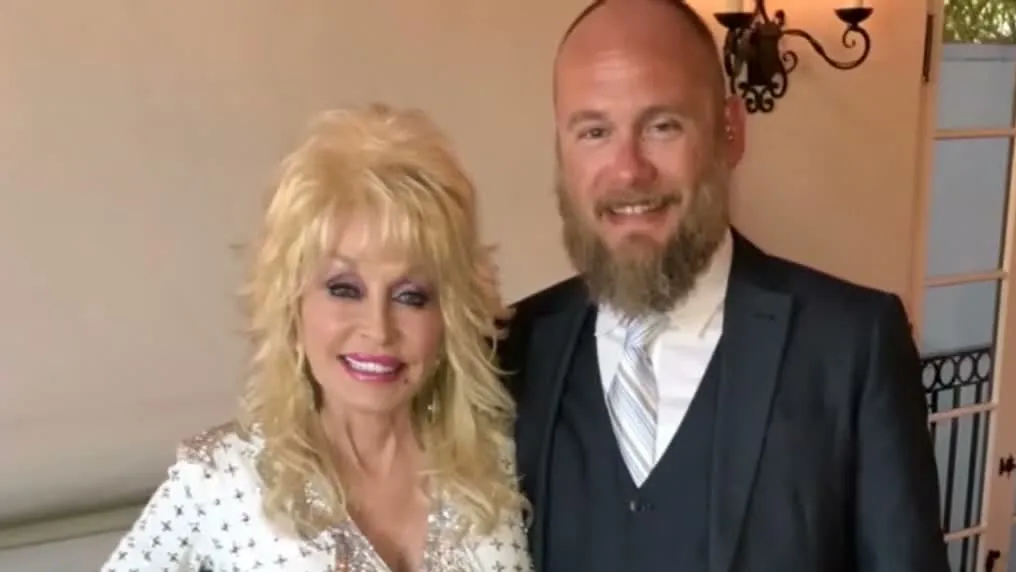 Dolly Parton smiling beside her nephew Bryan Seaver, who wears a dark three-piece suit