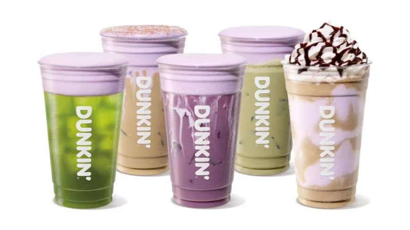 Five Dunkin' Halloween drinks topped with purple marshmallow cold foam: a green Sour Apple Energy, a Terror-misu Cloud Latte dusted with cocoa, a purple Dark Spell Daydream Refresher, a Franki Matcha and a Creepy Crawler Coffee Chiller with whipped cream and mocha drizzle