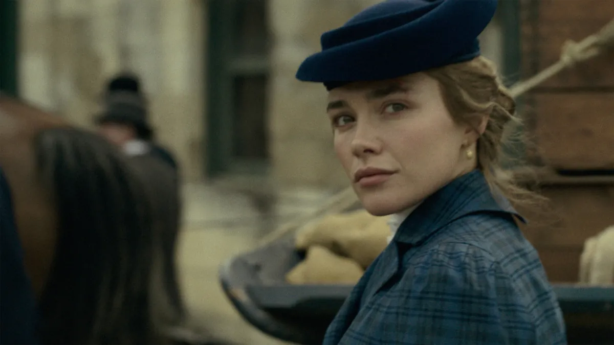Florence Pugh as Cathy Ames in a navy hat and plaid coat looking over her shoulder on a period street in East of Eden