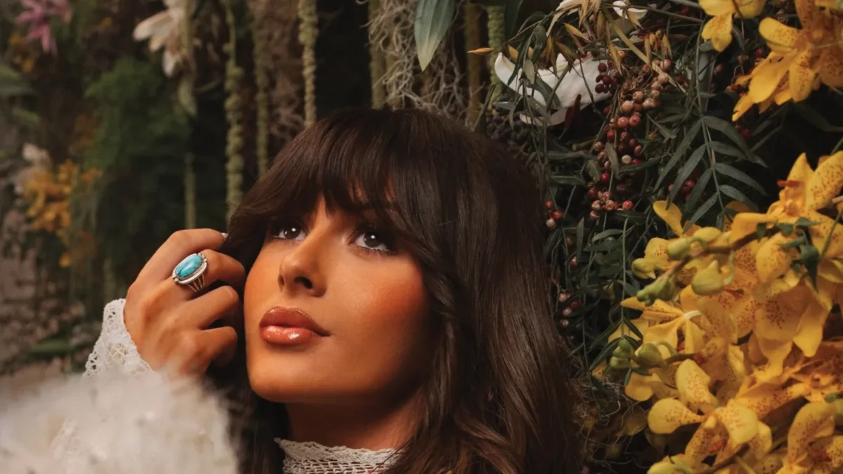 Ella Langley, with long dark hair and bangs and a turquoise ring, looks up among flowers and dandelion puffs on the cover of her album Dandelion