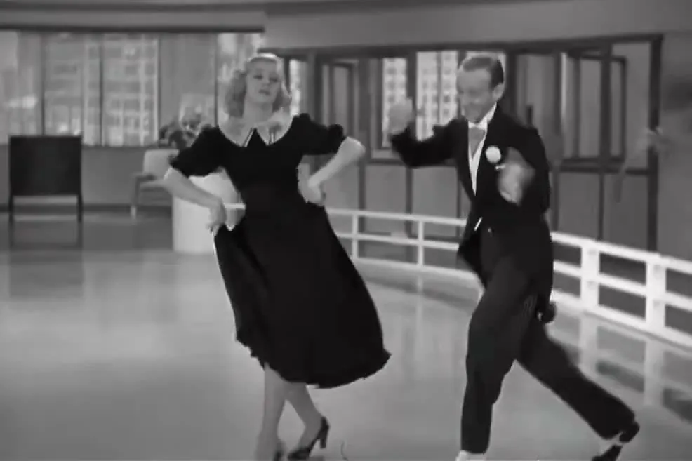 Ginger Rogers in a dark dress and Fred Astaire in a tailcoat dancing across a dance studio floor in the 1936 film Swing Time