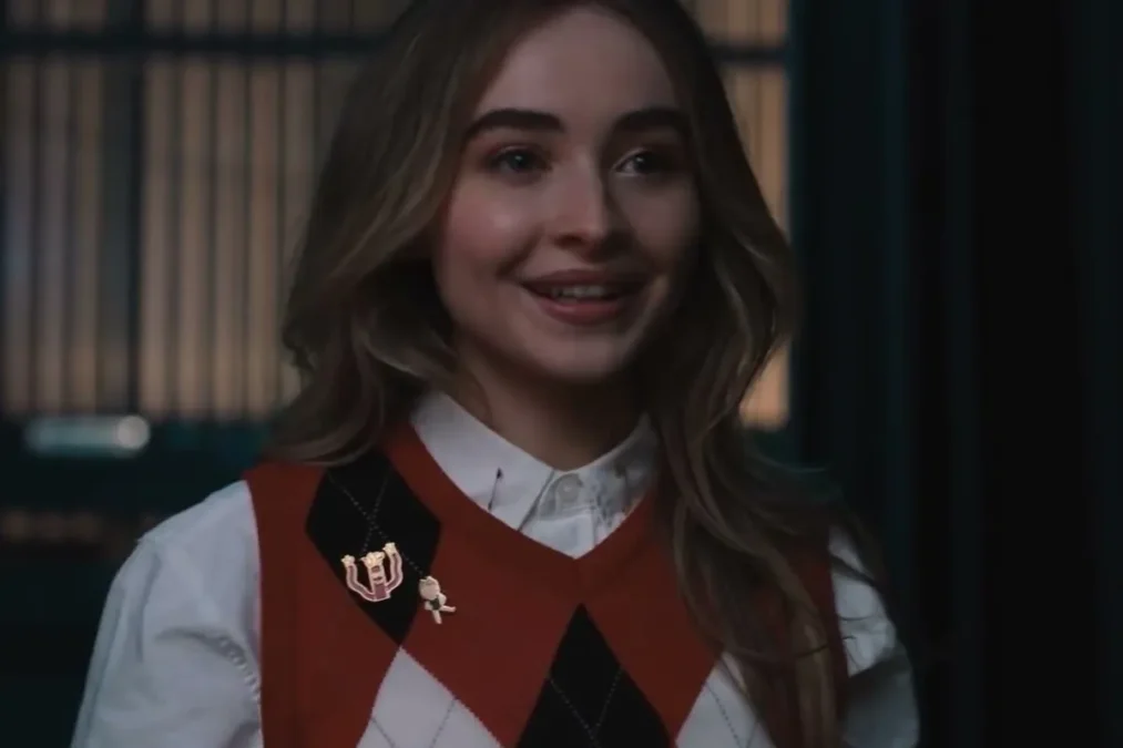 Sabrina Carpenter smiling in a red argyle sweater vest and white shirt in the Netflix film Work It