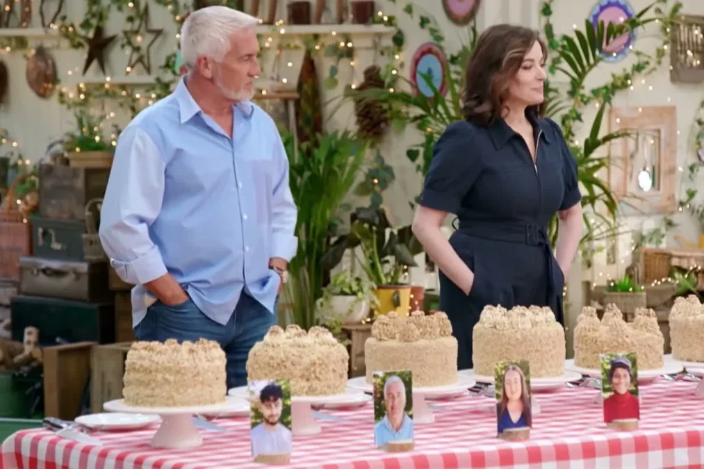 Paul Hollywood and Nigella Lawson standing behind a table of layer cakes in the Great British Baking Show tent