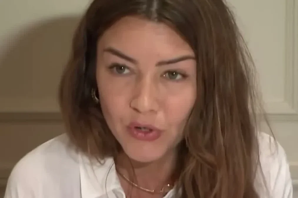 Miriam Haley, with long brown hair and a white blouse, speaking at a news conference