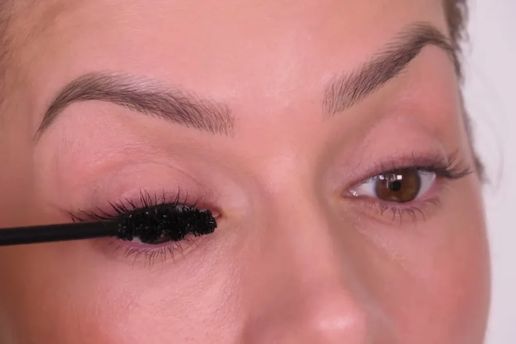 A mascara wand coating the upper lashes of one eye from the root outward