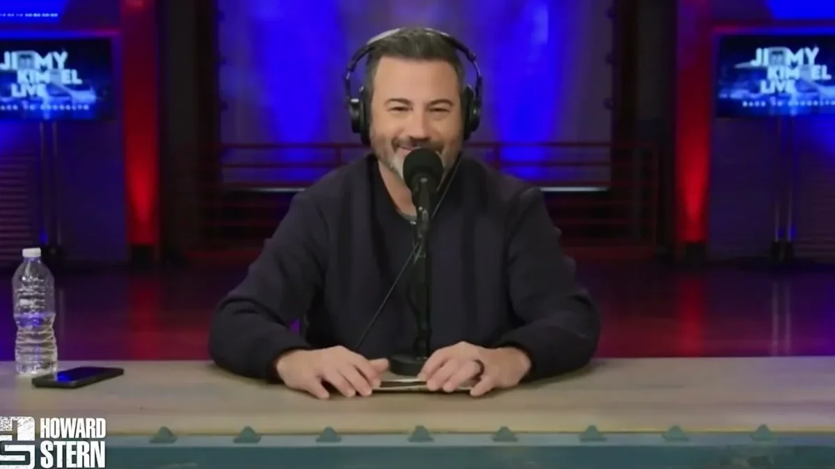Jimmy Kimmel wearing headphones and smiling behind a microphone at a desk