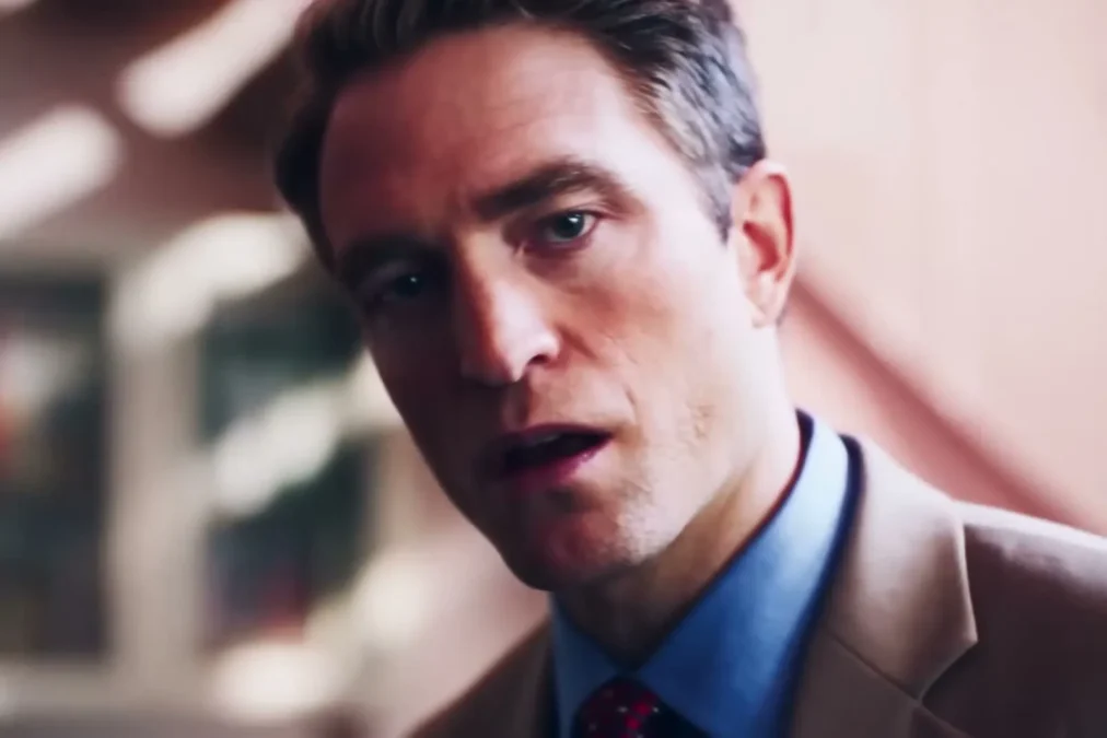 Robert Pattinson as Chris Hansen in a tan suit and red tie in a pink living room in Primetime