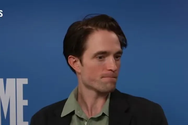 Robert Pattinson in a dark jacket and green shirt during a press interview in front of a Primetime backdrop
