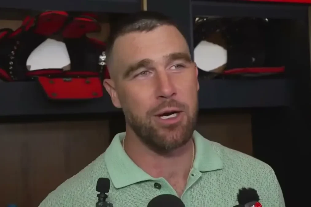 Travis Kelce in a mint green polo talking to reporters at his locker in Kansas City