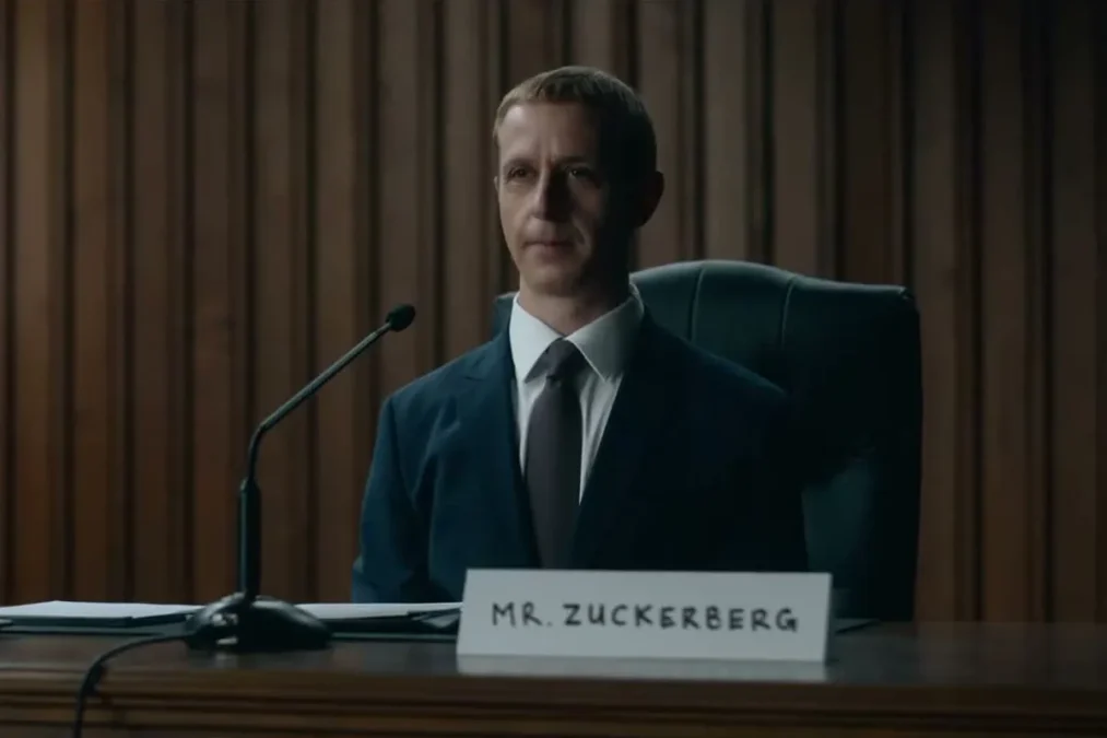 Jeremy Strong as Mark Zuckerberg seated at a hearing table behind a microphone and a placard that reads Mr. Zuckerberg
