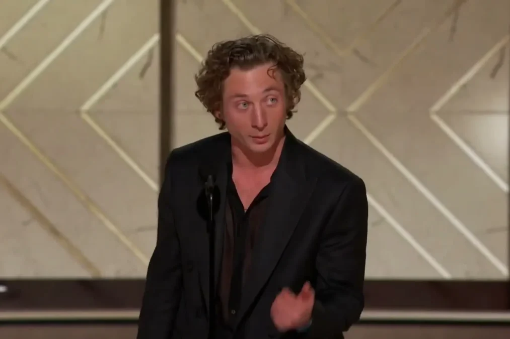 Jeremy Allen White speaking at a microphone on the Golden Globes stage in a dark suit