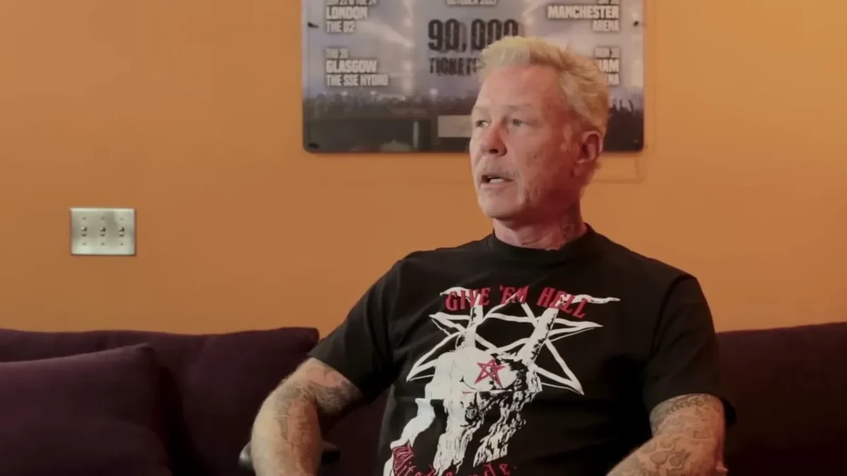 James Hetfield with short gray hair in a black graphic T-shirt sitting on a purple couch during an interview