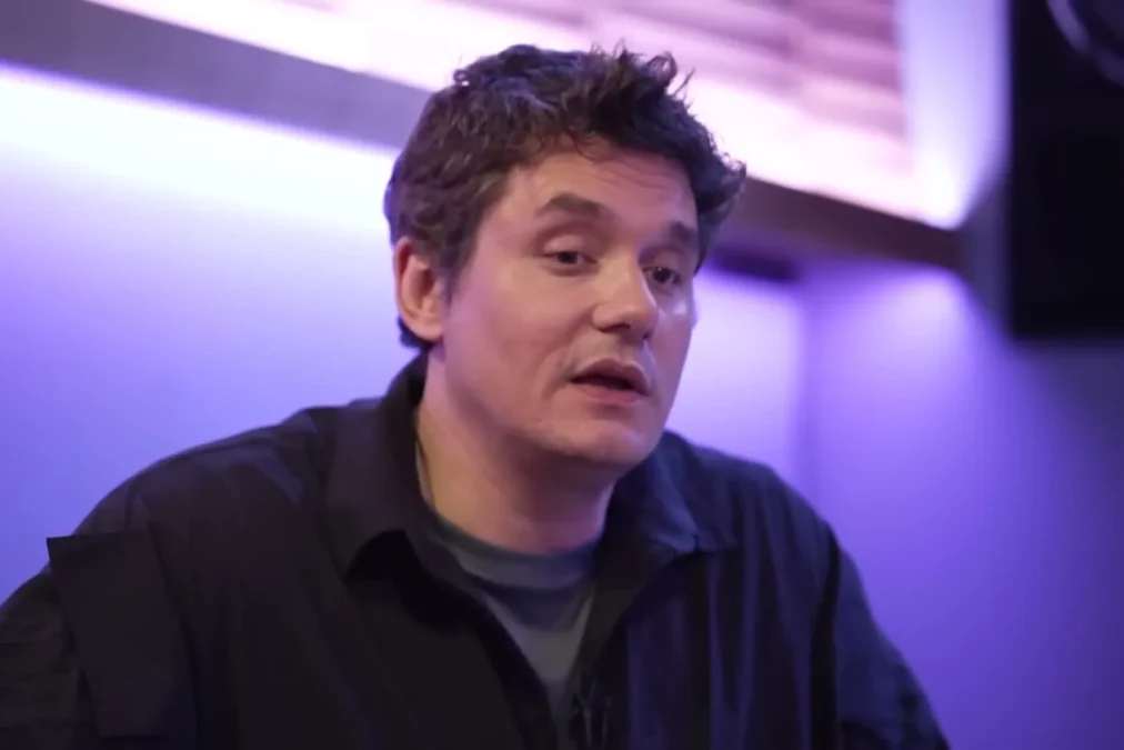 John Mayer in a dark shirt talking in a purple-lit room during a CBS Sunday Morning interview