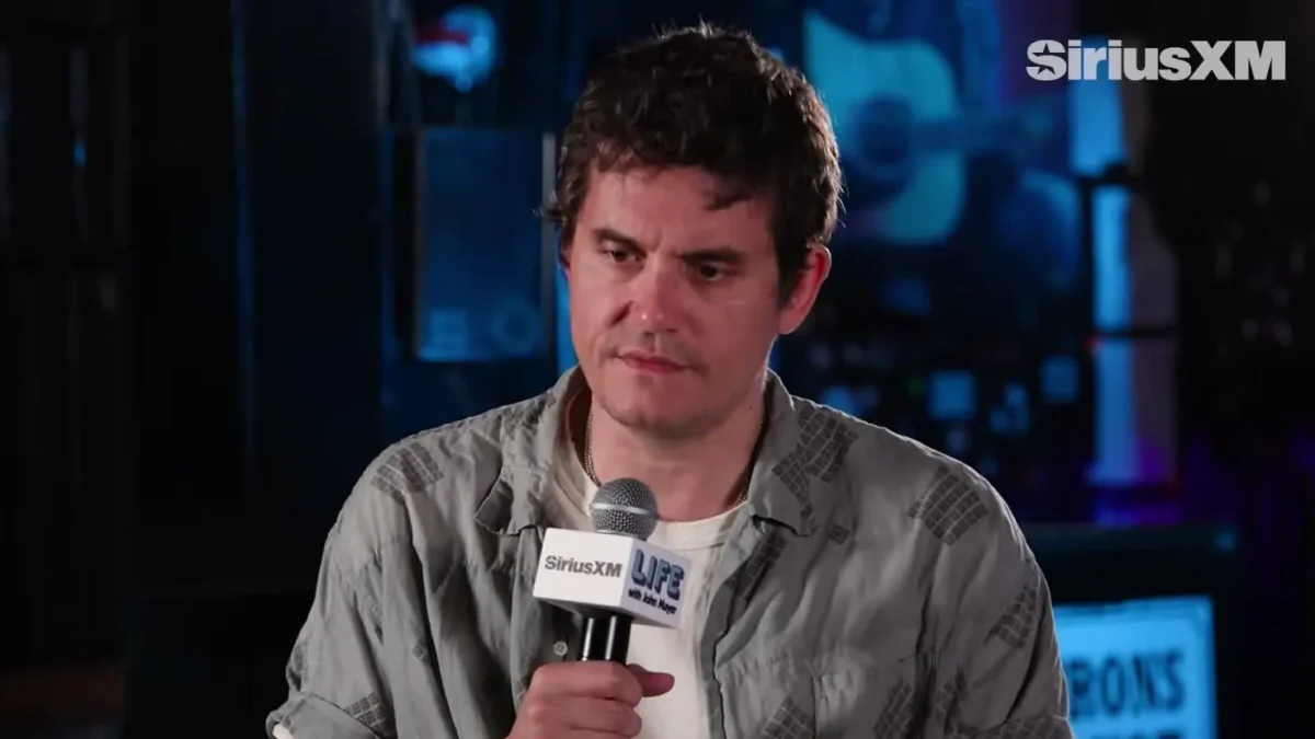 John Mayer in a gray short-sleeve shirt holding a microphone during a SiriusXM interview
