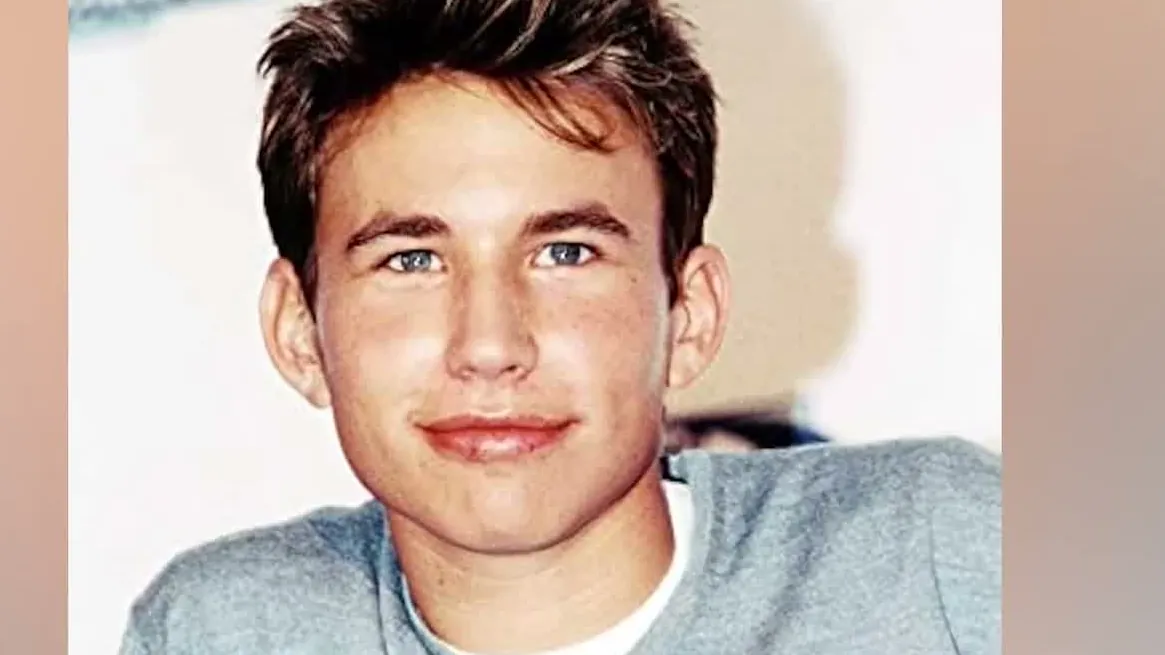 Jonathan Taylor Thomas as a teenager in a gray sweater, smiling at the camera