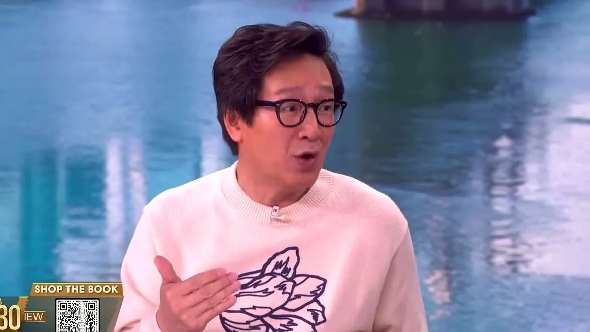 Ke Huy Quan in glasses and a cream sweater, speaking during an interview on The View