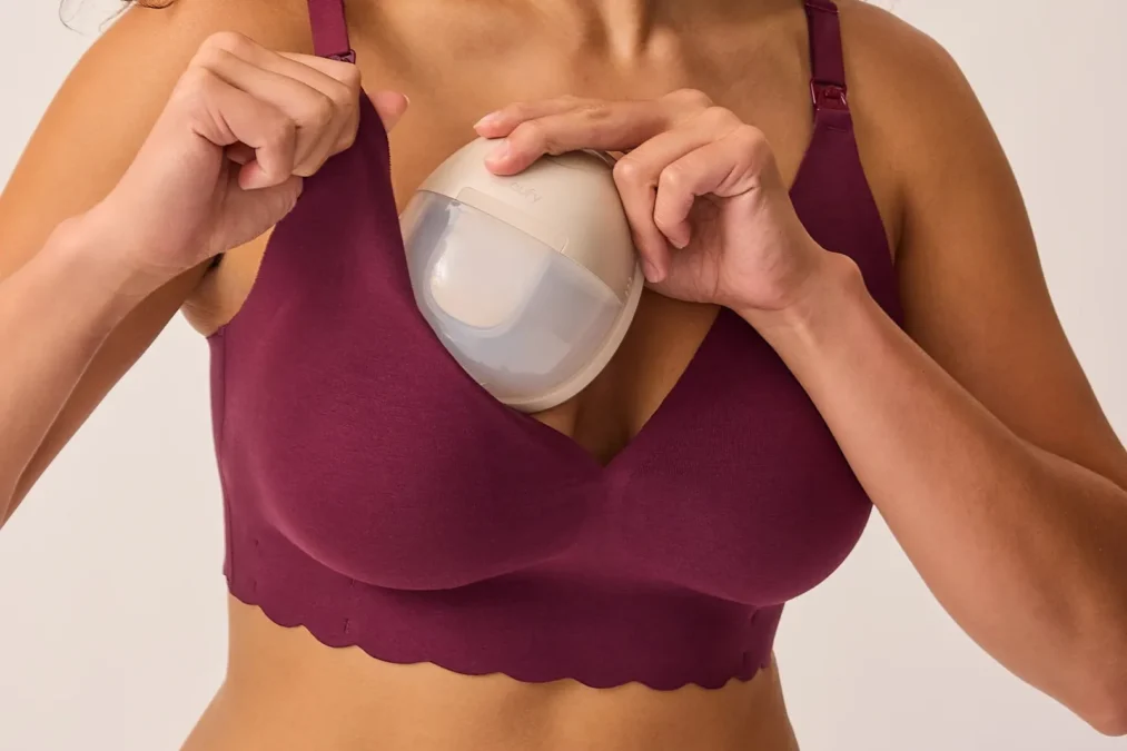 A woman fitting a wearable breast pump inside the cup of a garnet BareBond nursing bra