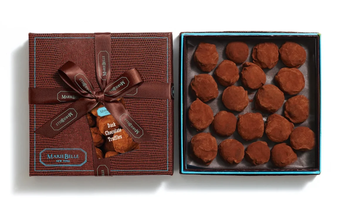 MarieBelle New York's 20-piece Dark Chocolate Truffle Box: a brown embossed box tied with a ribbon beside an open box of cocoa-dusted truffles