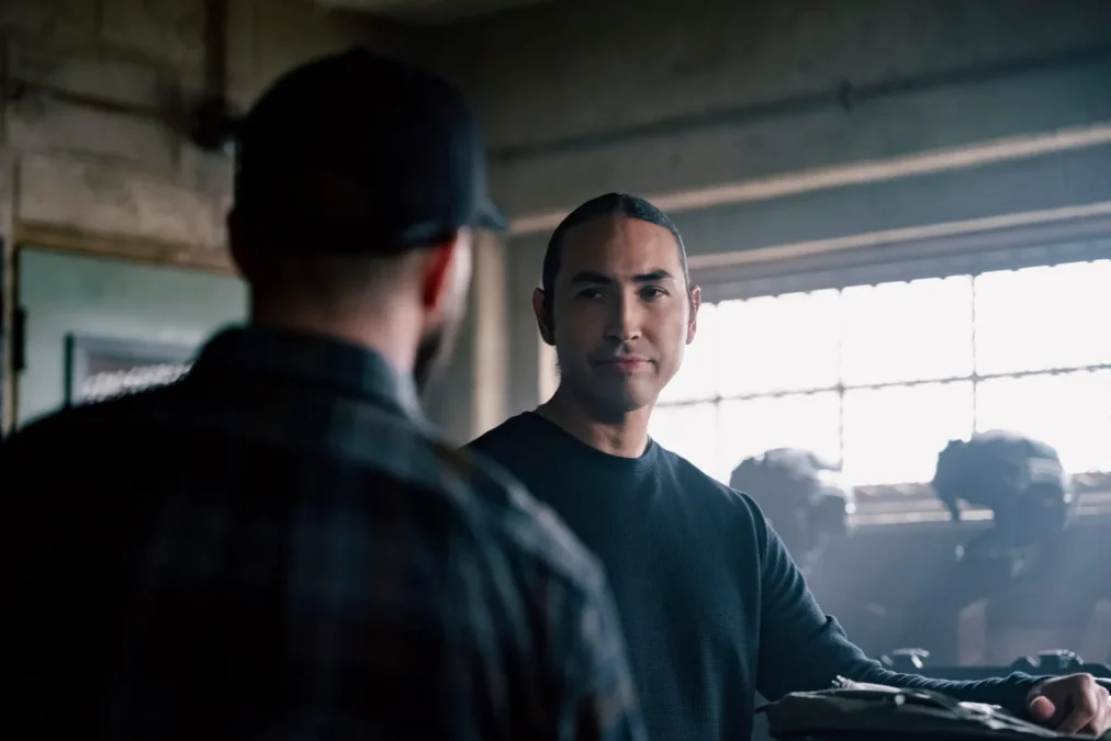 Tatanka Means as Miles Kittle talking with a man seen from behind in a sunlit office