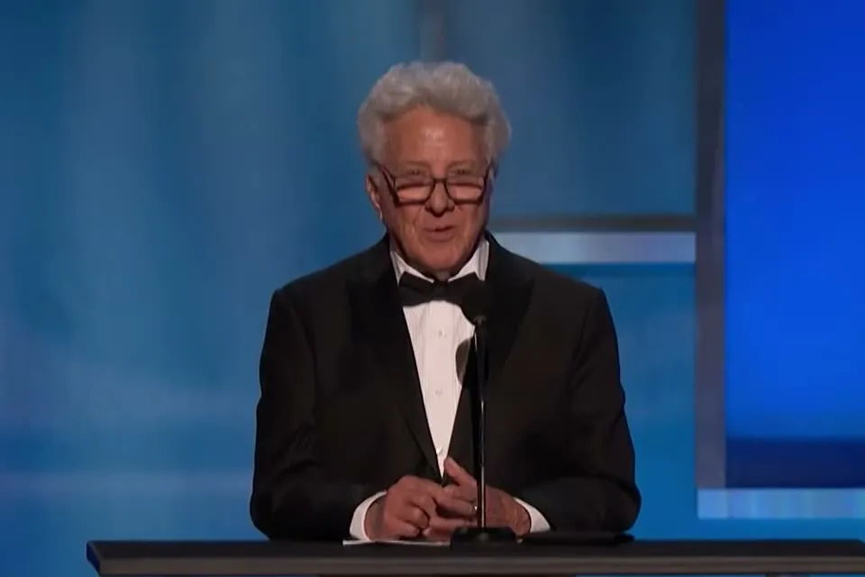 Dustin Hoffman in a tuxedo speaking at a microphone during an AFI Life Achievement Award tribute