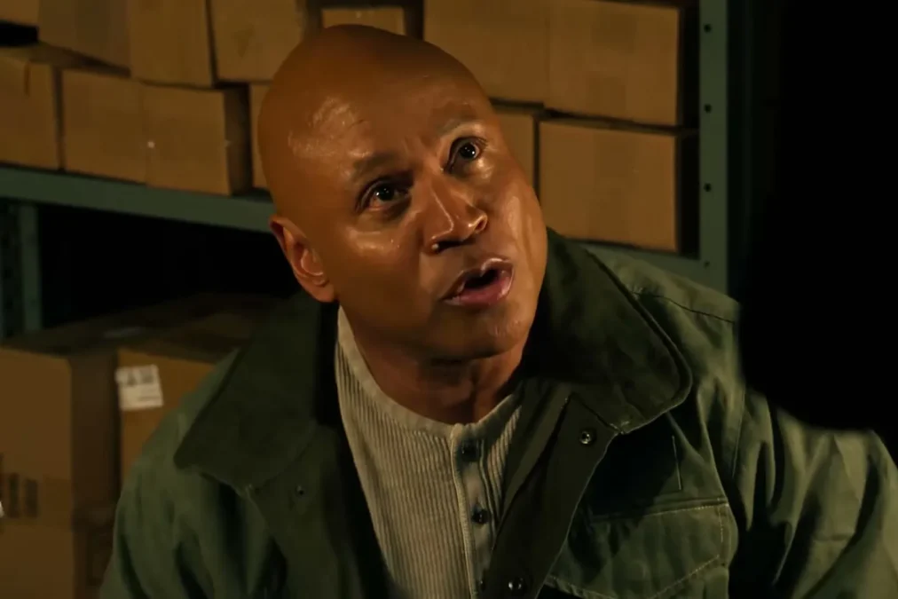 LL COOL J in a green jacket looking up in a dim room lined with cardboard boxes