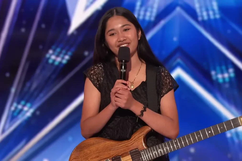 Nene Royal smiling and holding a microphone and an electric guitar on the America's Got Talent audition stage