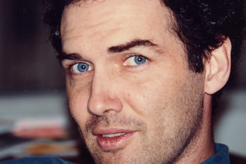 Archival close-up portrait of Norm Macdonald with dark curly hair and blue eyes