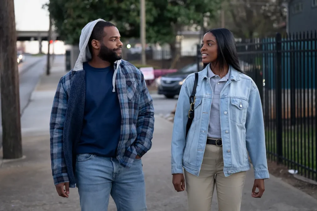 A man in a hoodie and plaid shirt and a woman in a denim jacket walk down a city sidewalk in Tyler Perry's Doing Life