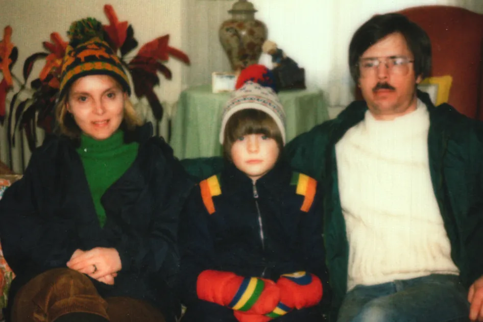 Vintage family photo of a woman, a child in a knit hat and a man in glasses on a patterned couch