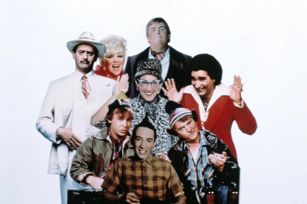 Vintage cast photo of SCTV, with performers in costumes posing against a white background