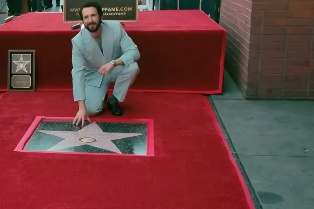 Josh Groban in a light blue suit kneeling on a red carpet beside his star on the Hollywood Walk of Fame