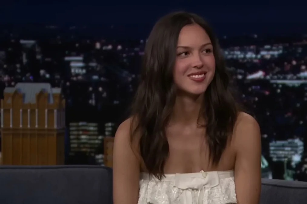 Olivia Rodrigo smiling on the Tonight Show couch in a white strapless dress