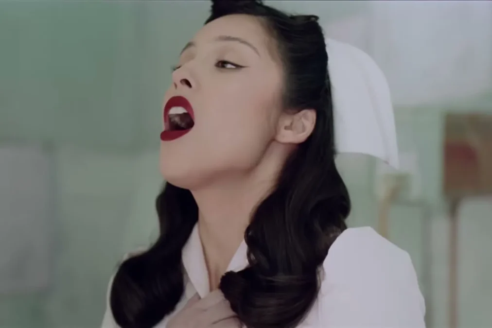 Olivia Rodrigo dressed as a 1950s nurse with red lipstick, singing in a hospital room