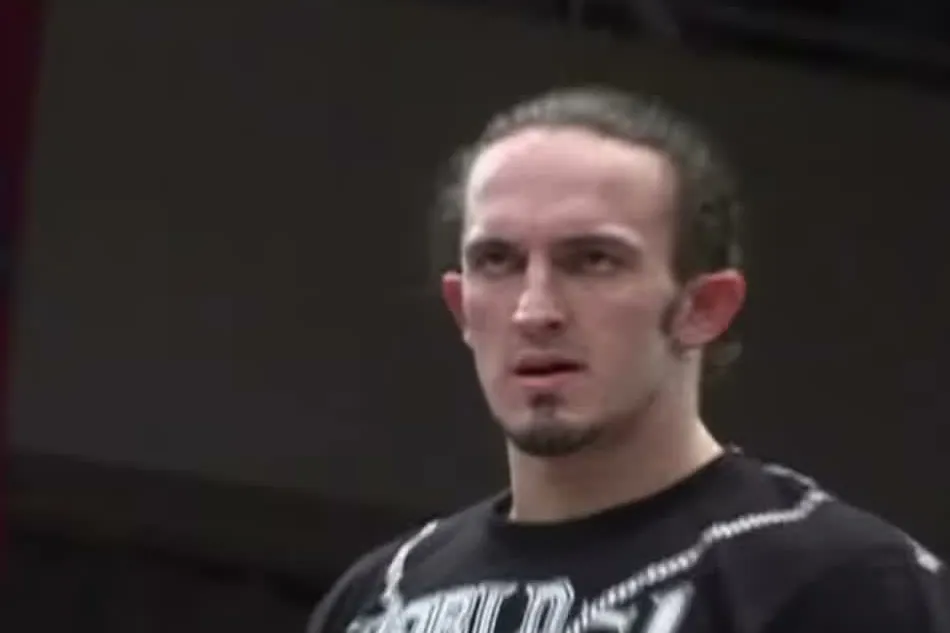 A young PAC in a black World-1 T-shirt, standing in a Dragon Gate arena in Japan