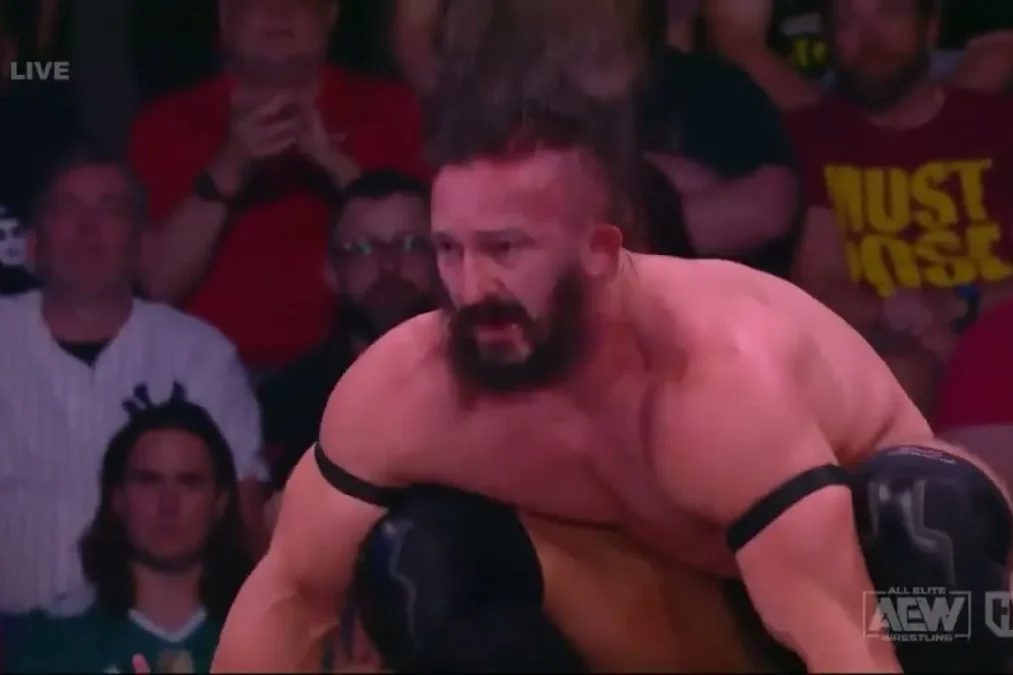 PAC crouching in the ring on AEW TV, with fans in the front row behind him
